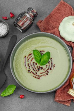 Fesleğen ve balzamik jöleli kremalı kabak çorbası taze malzemeler ve baharatlarla moda bir kasede servis ediliyor. Koyu taş zemin, üst görünüm