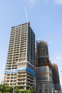 Vinçlerin alçak açılı görüntüsü ve bina inşaatının çelik yapıları mavi gökyüzü arka planına sahip..