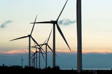 Tayvan 'ın batı kıyısında mavi gökyüzü arka planına sahip rüzgar enerjisi sistemlerinin gün batımı görüntüsü.