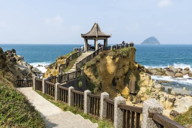 Turistler Keelung, Tayvan 'daki Heping Adası Parkı' ndaki Manzaralı Pavyon 'dan kayalık kıyı manzarasını ziyaret ederken, Keelung Adası hemen arkasında yer alıyor..