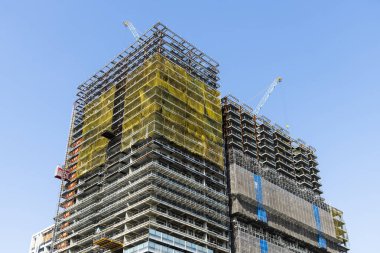 Vinçlerin alçak açılı görüntüsü ve bina inşaatının çelik yapıları mavi gökyüzü arka planına sahip..