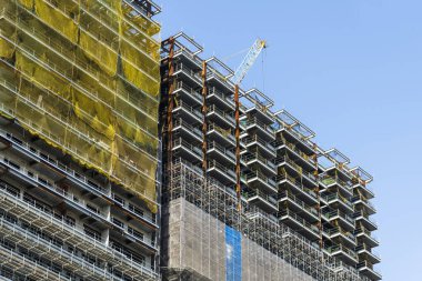 Vinçlerin alçak açılı görüntüsü ve bina inşaatının çelik yapıları mavi gökyüzü arka planına sahip..