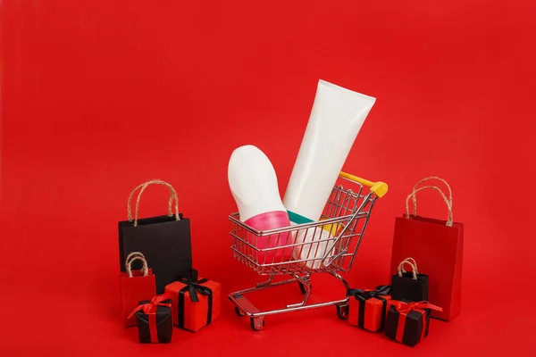 Shopping paper bags with trolley full skin care products on red background. Black friday concept. Sale and discount