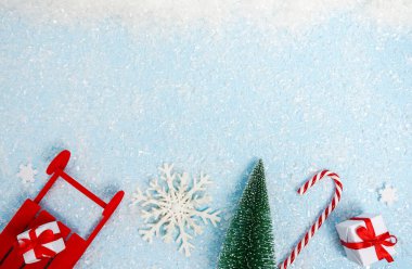 İçinde beyaz hediye kutuları, kar tanesi, kırmızı kızak, şeker ve Noel ağacı olan Noel tebrik kartı. Kopyalama alanı olan mavi kar arkaplanı