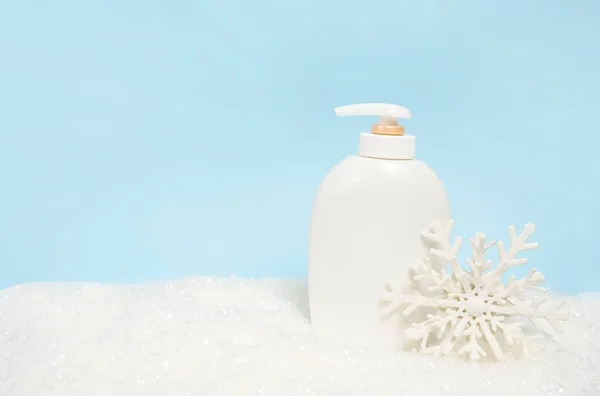 Cosmetic product bottle lotion or shampoo on blue christmas background with snow and big snowflake. Winter skin care