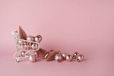Pembe arka planda noel süslemeleri ve fotokopi alanı olan beyaz alışveriş arabası. Noel alışveriş konsepti