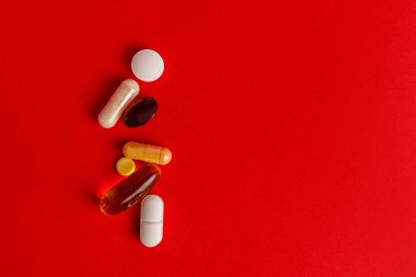 İlaç hapları, haplar ve gölgeli kapsüller kırmızı arka planda, boşluğu kopyala