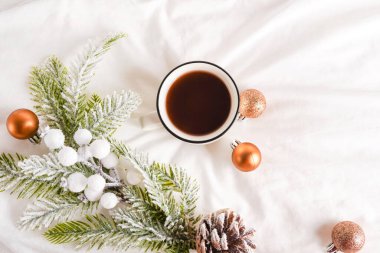 Beyaz yatağın üzerinde Noel süsleri olan kahve fincanı. Yatakta kahvaltı. Kış sabahı