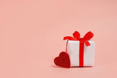 White gift box with red bow and heart on pink background with copy space