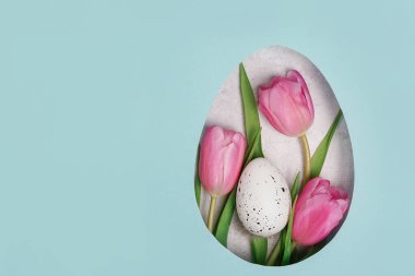 Easter layout with pink tulips flowers, blue paper background with copy space. Spring natural concept. Egg shape Easter holiday minimal composition. Flat lay