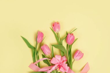 Pink tulips bouquet, wrapped with pink ribbon over yellow background. Copy space