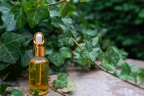 Golden glass bottle with cosmetic product oil or serum on a natural green background with leaves