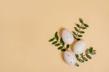 Easter eggs and green branches on beige background with copy space
