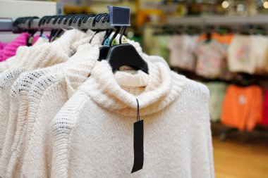 Stylish clothes on hangers in the store, white sweaters