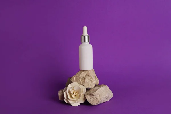 stock image Glass dropper bottle with cosmetic oil, essential or serum staying on stone stand with dry flower on violet background. Herbal homeopathic products Natural organic spa cosmetics