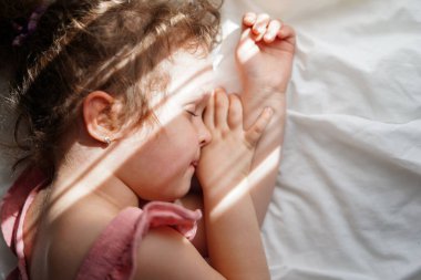 Sevimli küçük kız evde güneş ışığıyla yatakta uyuyor.