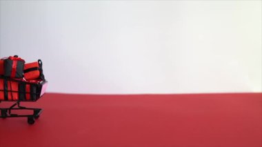 Kırmızı ve beyaz arka planda alışveriş arabasında siyah hediye kutuları. Kara Cuma