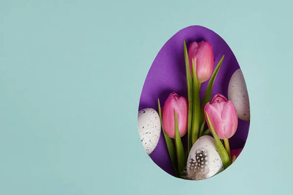 Easter egg with pink tulips and white eggs, blue paper background, copy space
