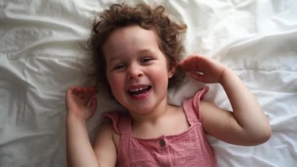 Pembe Elbiseli Kıvırcık Saçlı Gülümseyen Evde Yatakta Uzanan Mutlu Kız — Stok video
