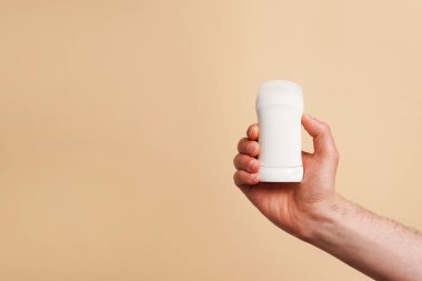 Bej arka planda beyaz deodorant tutan bir erkek. - Yakın çekim. Boşluğu kopyala