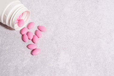 Beyaz şişeden akan pembe haplar hafif beton arka planda, ilaç