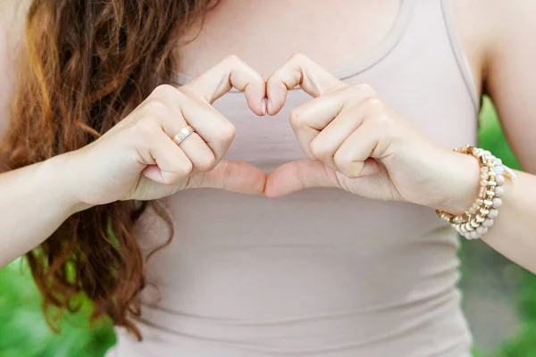 Woman in beige clothes with long hair Holding Heart Shaped Hands. Showing Love Sign