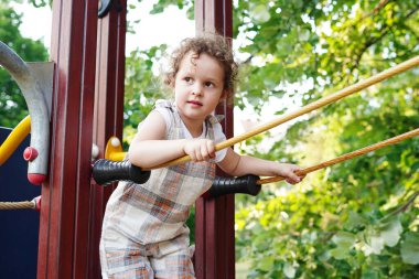 Sıcak bir yaz gününde çocukların oyun parkında oynayan kıvırcık saçlı küçük tatlı kız, çocuklar için eğlence ve eğlence.
