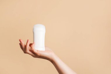 Kadın eli bej arka planda beyaz vücut deodorantı tutuyor, boşluğu kopyala