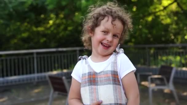 快乐的小女孩 卷发在公园里 在阳光下 孩子们的脸上洋溢着欢乐的光芒 小孩对着相机笑 — 图库视频影像