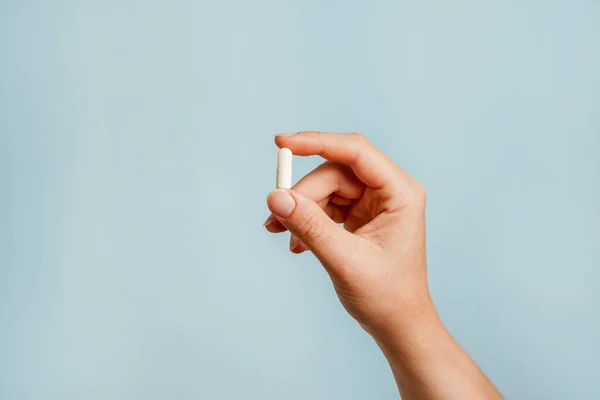 stock image White pill in female hand on blue background, Taking Your Medication