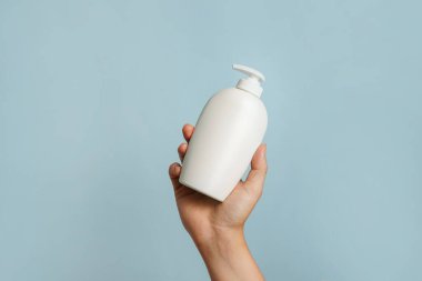 Elinde beyaz losyon şişesi, sabun ya da şampuan tutan bir kadın.