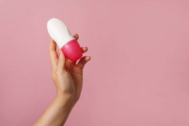 Kadın eli pembe arka planda vücut deodorantı tutuyor, boşluğu kopyala