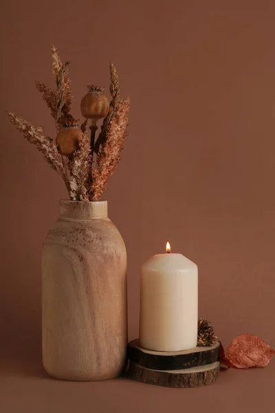 Autumn dried flowers in the vase and vanilla candle on brown background. Warm aesthetic autumn composition. Home comfort, spa, relax and wellness concept