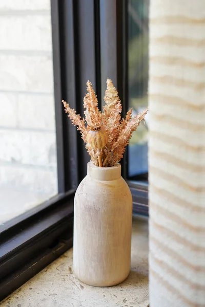 Dried flowers in wooden vase staying on the window sill. cozy home, autumn decoration