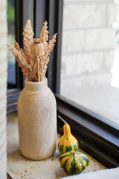 Dried flowers in wooden vase and pumpkins on the window sill. cozy home, autumn decoration