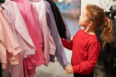 Şirin kız alışveriş merkezinde süveter seçiyor.