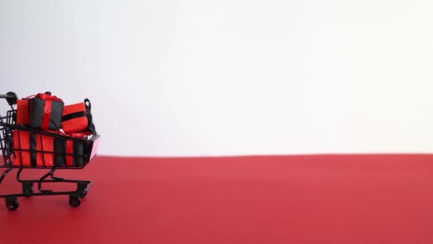 Zwarte Winkelwagen Met Kleine Geschenkdoosjes Witte Rode Achtergrond Kopieerruimte Zwart — Stockvideo