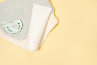 Beyaz krem tüpü ve bebek emziği sarı masa arkasında. Temiz ve yumuşak vücut cildine dikkat et. Günlük çocukların güzellik ürünleri
