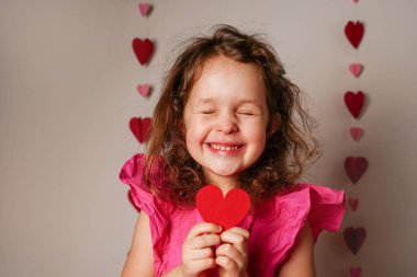 Pembe elbiseli küçük kız elinde kırmızı bir kalp ve kahkahalar