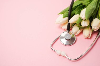 Pembe arka planda steteskoplu beyaz laleler. Ulusal Doktor Günü. Hemşire günün kutlu olsun. Kopyalama alanı olan üst görünüm