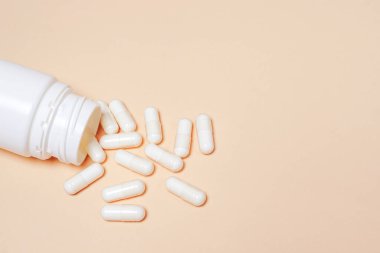 Bej arka planda ilaç kutusundan çıkan beyaz haplar ve fotokopi alanı. Beyaz haplar.