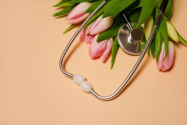 Bej arkaplanda steteskop ve pembe laleler.