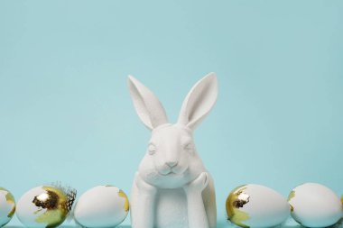 Paskalya mavisi arka plan, beyaz tavşan ve altın parıltılı yumurtalar, kopyalama alanı. Paskalya tebrik kartı