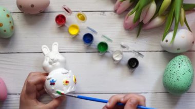 Paskalya tavşanını boyayan çocuk, lale ve yumurtalarla dolu ahşap masa.
