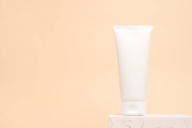 Taş podyumda kalan beyaz kozmetik tüp, kopya alanı olan bej arkaplan
