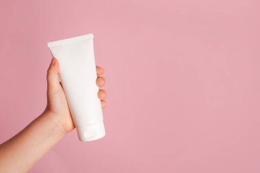 Küçük bir el pembe arka planda beyaz krema tüpü tutuyor. Günlük çocukların güzellik ürünleri. - Yakın çekim. Metin veya logo için boş yer