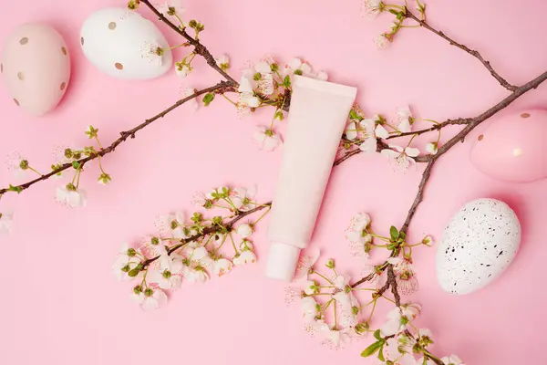 Cosmetic cream or Foundation beige tube on pink background with Easter eggs and spring flowers