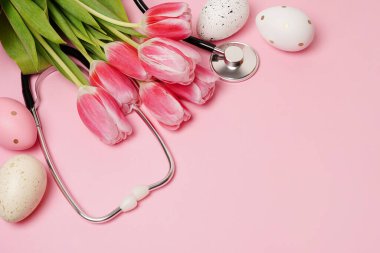 Paskalya yumurtalarıyla steteskop ve pastel arka planda fotokopi alanı olan pembe laleler.