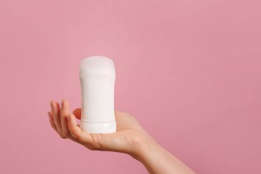 Pembe arka planda beyaz deodorant tutan bir kadın. - Yakın çekim. Boşluğu kopyala