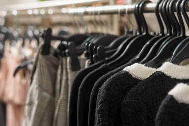 Bir mağazada elbise askısı, siyah askılara düzgün asılmış siyah ve damalı giysiler sergileniyor.